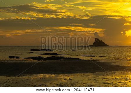 Beautiful sea sunset with small island silhouette on the beach at low tide & reflections in the sand.