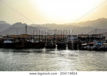 View on a boats docked at the little harbour in Oman beautiful sunset over Al Hajar Mountains