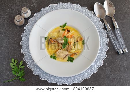Creamy soup with fish fillet and mussels in a white plate on a white cloth on a grey abstract background. Healthy eating concept. Mediterranean lifestyle