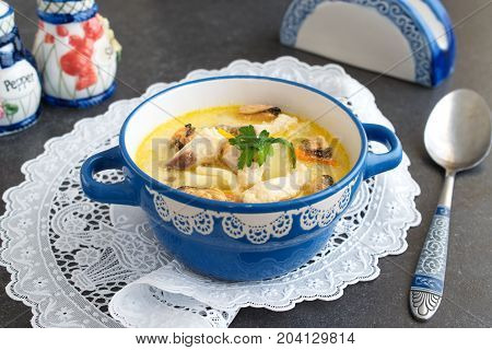 Creamy soup with fish fillet and mussels in a blue ceramic pot on a white cloth on a grey abstract background. Healthy eating concept. Mediterranean lifestyle.
