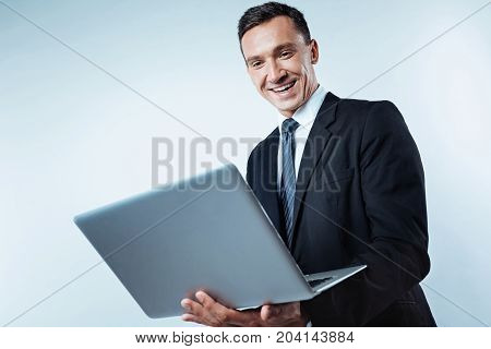 Positive attitude to work. Low angle shot of an excited mature entrepreneur looking at a screen of a computer with a wide smile on his face while working over the background.