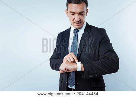 What time is it now. Waist up shot of a successful man looking at a dial of his wrist watch while standing over the background and rushing for work.