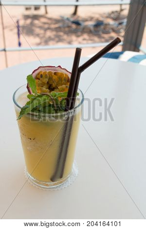 A glass of passion fruit smoothie on table at beach cafe.