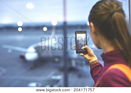 Girl at the airport window looking outside and photographing a plane