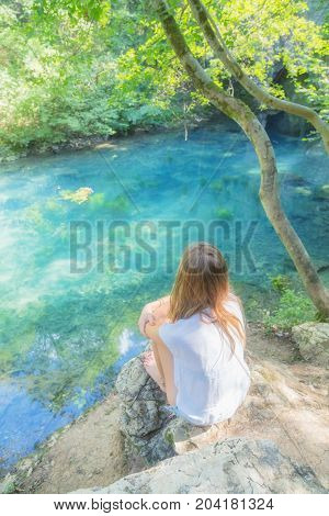 Young woman sitting near the beautiful lake in nature.