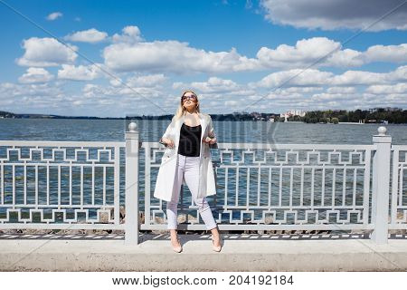 Pretty Young Blonde Woman Standing At The Embankment Seashore In The Rays Of The Setting Sun