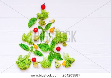 Healthy new year concept - Collection of fresh organic vegetables and greeens in form of christmas tree on white wooden background. Top view. Selective focus. space for text.