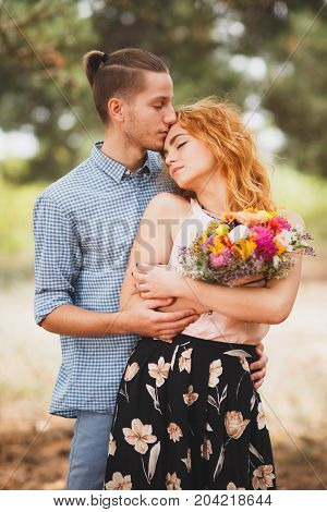 Image of love story in the forest. Beautifull couple kissing and embracing near the shore of a mountain river with decorated table. Girl smiling in the arms.