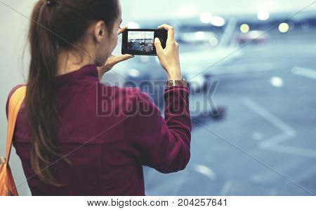 Girl at the airport window looking outside and photographing a plane