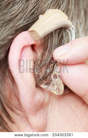 Closeup senior woman with hearing aid in her ear. Health care hear amplify device for the deaf.
