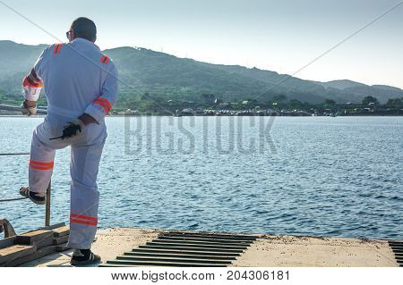 Ferryman on edge of deck. Ferry moving toward of shore.