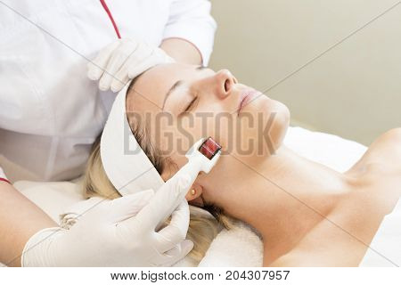 The woman undergoes the procedure of medical micro needle therapy with a modern medical instrument derma roller.