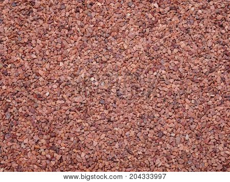 Close-up sand texture, modern coating for running tracks. Image of cover athletic fields in close proximity. A lot of small red glitter stones. Abstract orange color asphalt.