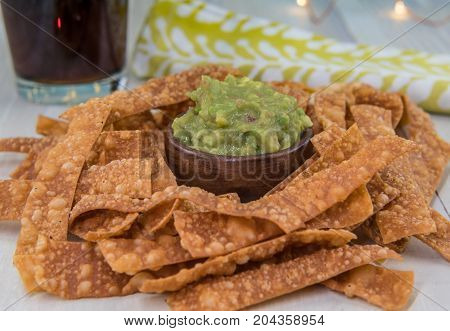 Bowl of Guacamole and Chips with Drink and Napkin in Background on light table top