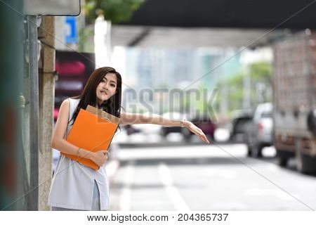 Asian Business woman hailing cab. Beautiful female is calling a taxi in a city. copy space.
