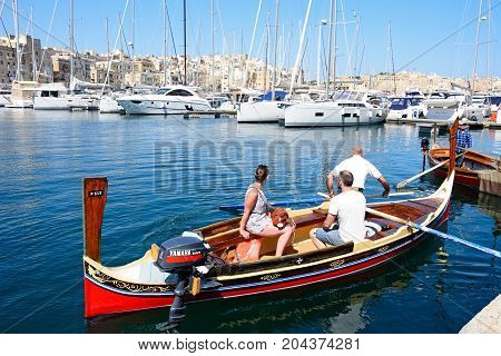 SENGLEA, MALTA - MARCH 31, 2017 - Passengers on board a traditional Maltese Dghajsa water taxi in the harbour with views towards Senglea waterfront Vittoriosa Malta Europe, March 31, 2017.