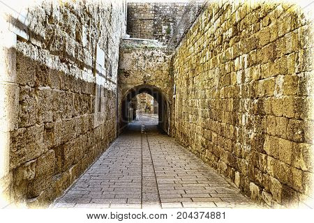 Narrow Alley in the old city of Akko in Israel. Cobbled street among traditional stoned houses in old Acre. Vintage style toned picture