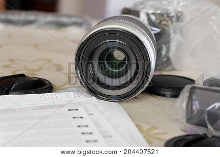 New camera lens with caps and instruction on the table. Background with limited depth of field.