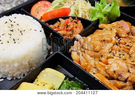 Traditional Japan Cuisine Bento Box or Multi-Layered Box with Teriyaki Chicken Rice Salad Tamagoyaki or Rolled Omelette Hiyashi Wakame or Seaweed Salad and Kimchi.