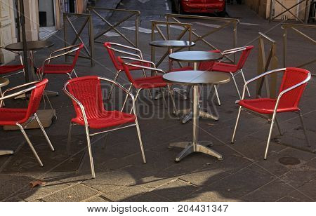 Gray round tables and red chairs in a cafe on the street in Antibes