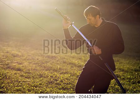 Ninja in black kimono is practicing martial arts with sword outdoors.