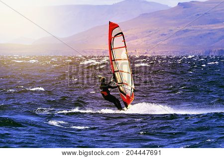 Sportman windsurfer on the lake surface at sunset time.