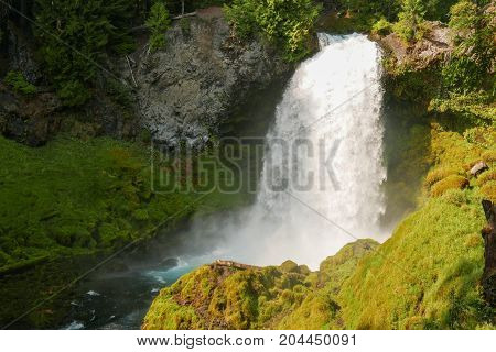 Horizontal shot of Sahalie waterfalls with river and bright green moss covered rocks and foliage