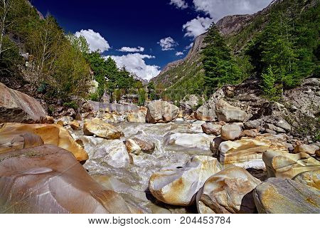 The Ganges River flows across the town. Houses in rocky river valley and green forest against snow capped mountain in the distant. Panoramic view of river. Gangotri. Uttarakhand. India.