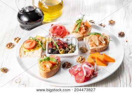 Selection of tasty bruschetta or canapes on taosted baguette and quark cheese topped with smoked salmon, shrimp, prawn, olives, tomato and chorizo sausage