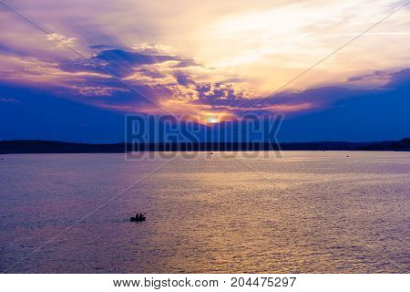 Two men paddling in an inflatable kayak in colorful sunset, clouscape, watersports, sea