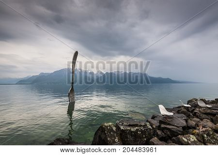 Vevey Switzerland - May 25 2016: Giant steel fork in water of Geneva lake in cloudy weather Vevey Switzerland.The fork went up in 1995 to mark the 10th anniversary of the Alimentarium Veveys Food Museum.