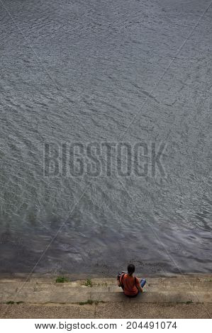 Young accordionist sitting on steps facing the river