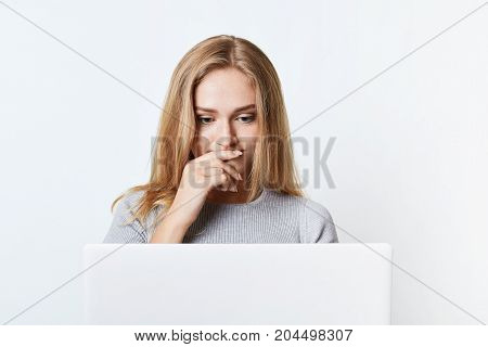 Puzzled Female With Beautiful Appearance Reads News Online, Being Focused On Laptop Computer. Young