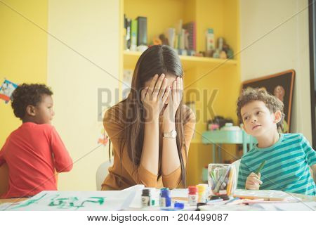 Asian teacher kindergarten hands closed both ears of her in an upset of failed to quell quited naughty of the boys in class at preschool kids argument. Vintage effect style pictures.