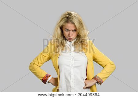 Portrait of dissatisfied young woman. Severe powerful frowning young woman holding hands on hips over gray background. Facial expression and body language.