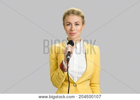 Young woman in formal wear with microphone. Young business woman public speaking isolated on grey background.