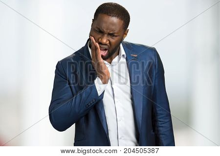Businessman feeling tooth pain. Upset young man with toothache. Black manager touching his cheek and feel pain.