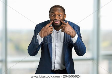 Black businessman with artificial smile. Businessman making a face at camera holding his fingers near lips.