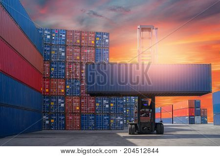 Forklift truck lifting cargo container in shipping yard or dock yard against sunrise sky with cargo container stack in background for transportation import, Export and logistic industrial concept