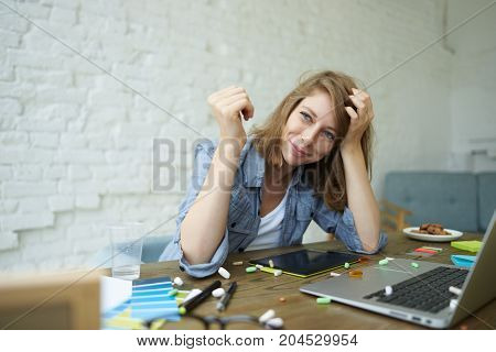 Picture of joyful ecstatic young Caucasian woman employee feeling euphoric after she took sedative drug sitting at her workplace using laptop computer colorful pills spilled all over desk