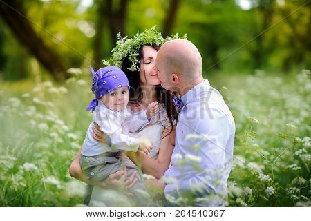 young family walks with kids in the beautiful park on a sunset amicably embrace and kiss mother on the head has a wreath from wild flowers