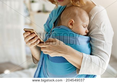 Cute tiny kid napping peacefully while mother hugging him and texting husband by phone asking buy some baby food and diapers. Lifestyle, family concept