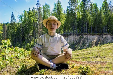A man in meditation in a yoga posture in nature. The boy sits Closing his eyes and enjoys the silence of the forest. Tranquility and serenity
