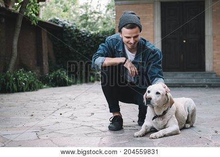 The ideal picture of a guy and his best friend - the golden labrador. The dog is laying on the ground while his owner is stroking a dog on the head. This gus is happy to be with his pet and smiling because of that.