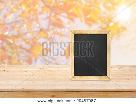Blackboard on wood table top with blur maple leaf with sunlight backgroundAutumn backdropMock up for display or montage of productbanner for advertise on online.