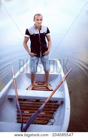 young man standing in the white boat, handsome teenager in light shorts and shirt, guy enjoys outdoor recreation