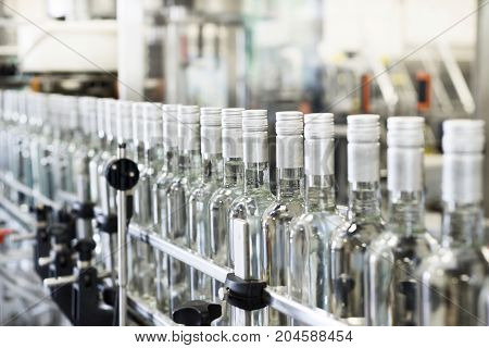 A long row of glass bottles on the conveyor. The bottles are closed with a screw cap.