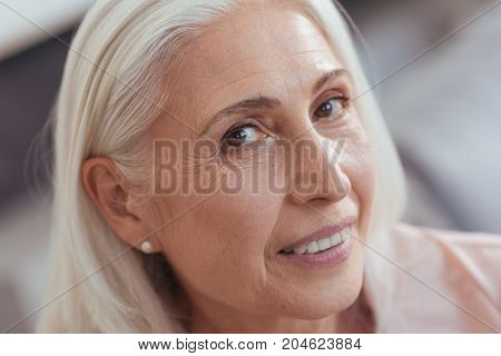 Surreptitious look. Close up of a pleasant aged woman smiling and expressing joy while looking at you