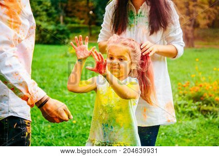 father mother and daughter full around with holi paints in city park