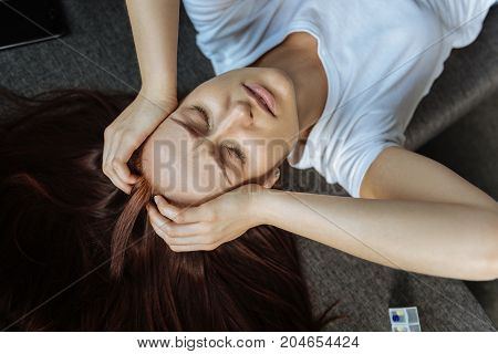 Unbearable pain. Top view of a sad unhappy suffering woman closing her eyes and holding her head while suffering from a headache